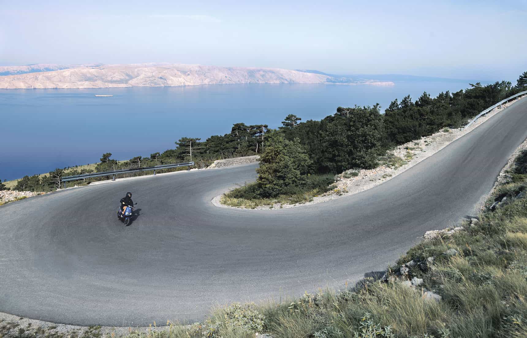 Motard sur une route côtière sinueuse au-dessus de la mer