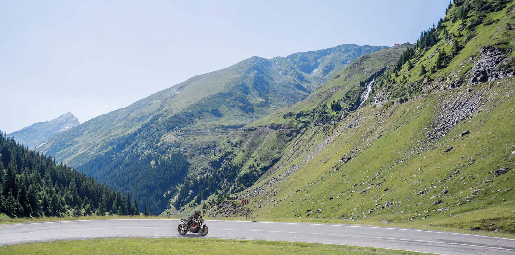 Motard sur une route alpine entre des montagnes verdoyantes