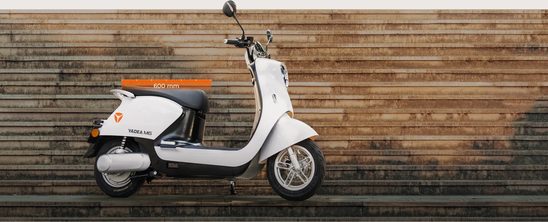 YADEA M6 blanc de profil devant un mur de bois ; une barre orange indique une selle de 600 mm